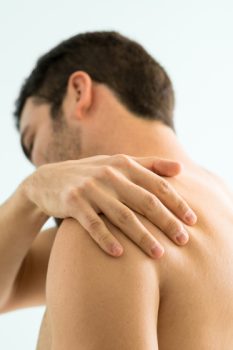 Shirtless young man suffering from muscle pain on his shoulder and visiting a spa to relieve it